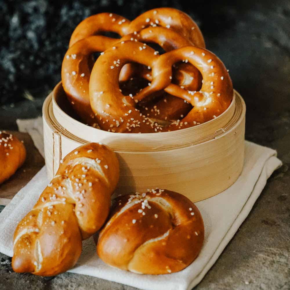 frische Brezeln und Laugenknoten in einem Holzkorb auf einem Weißen Geschirrtuch