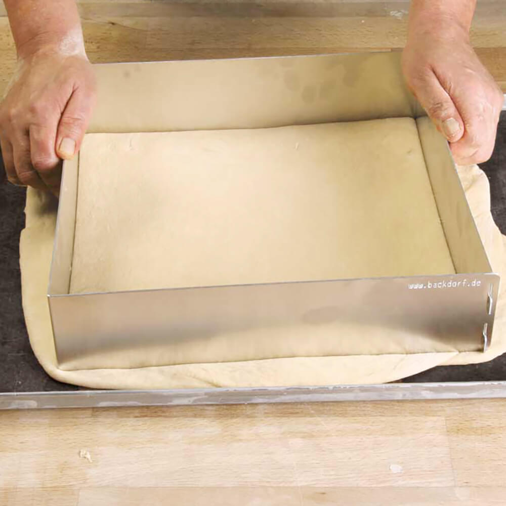 Ein Backrahmen wird auf einen ausgewellten Teig gelegt. Der Teig liegt auf einer Dauerbackfolie und diese liegt auf einem Blech