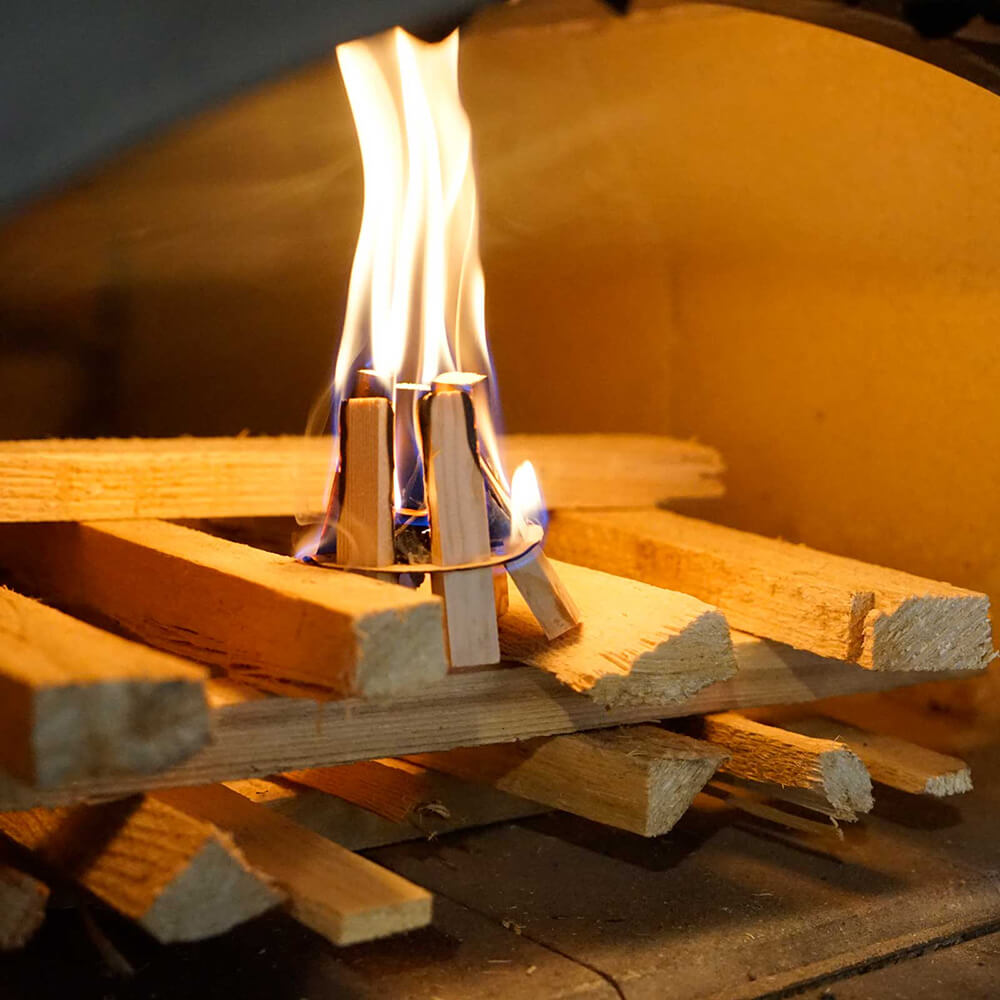 Gestapeltes Holz im Holzbackofen. Die Hölzer des Feuerkits gehen in Flammen auf