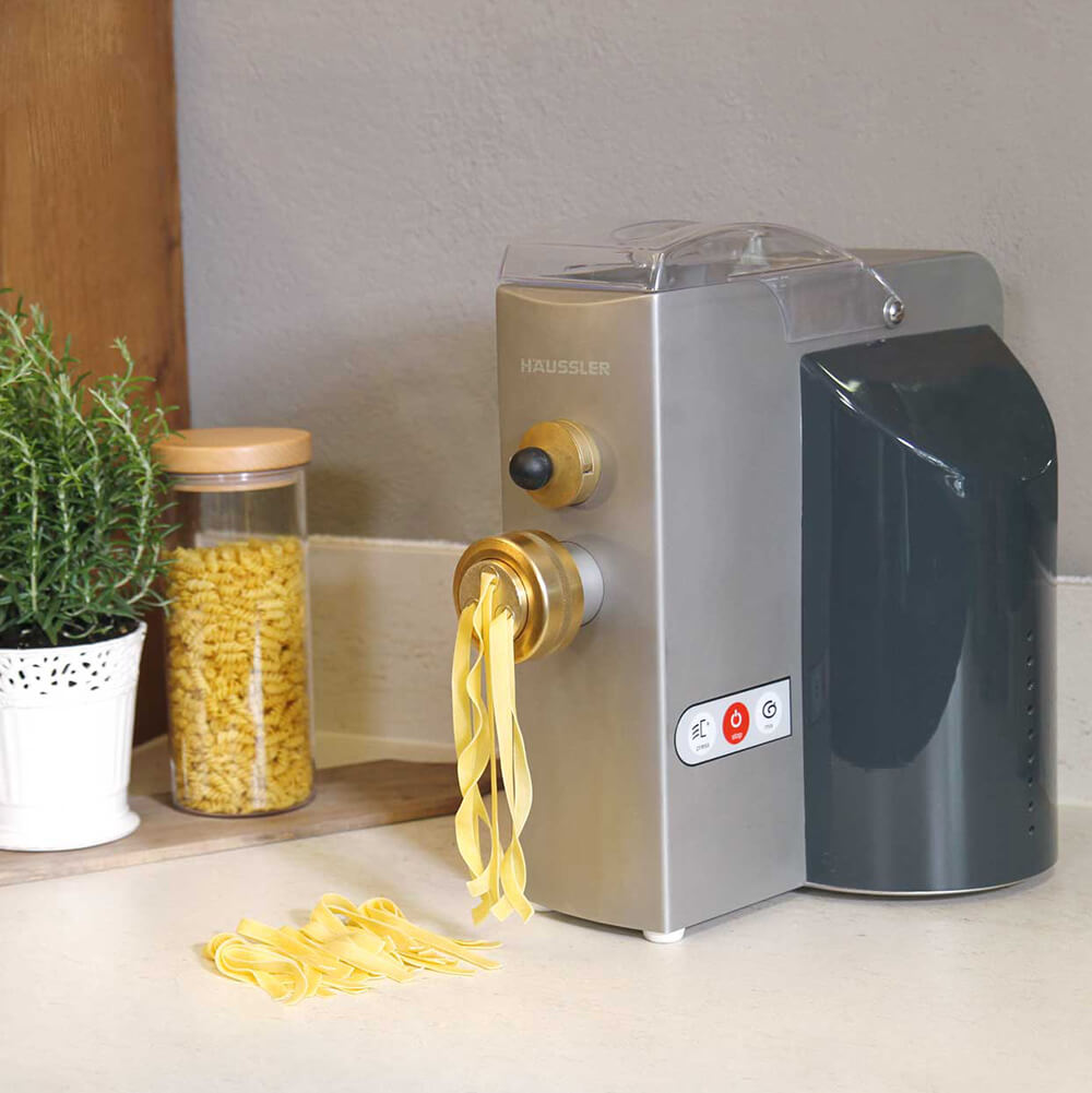 Nudelmaschine Emma Auf einer Arbeitsfläche steht eine Nudelmaschine. Aus dieser werden gerade Bandnudeln herausgepresst.