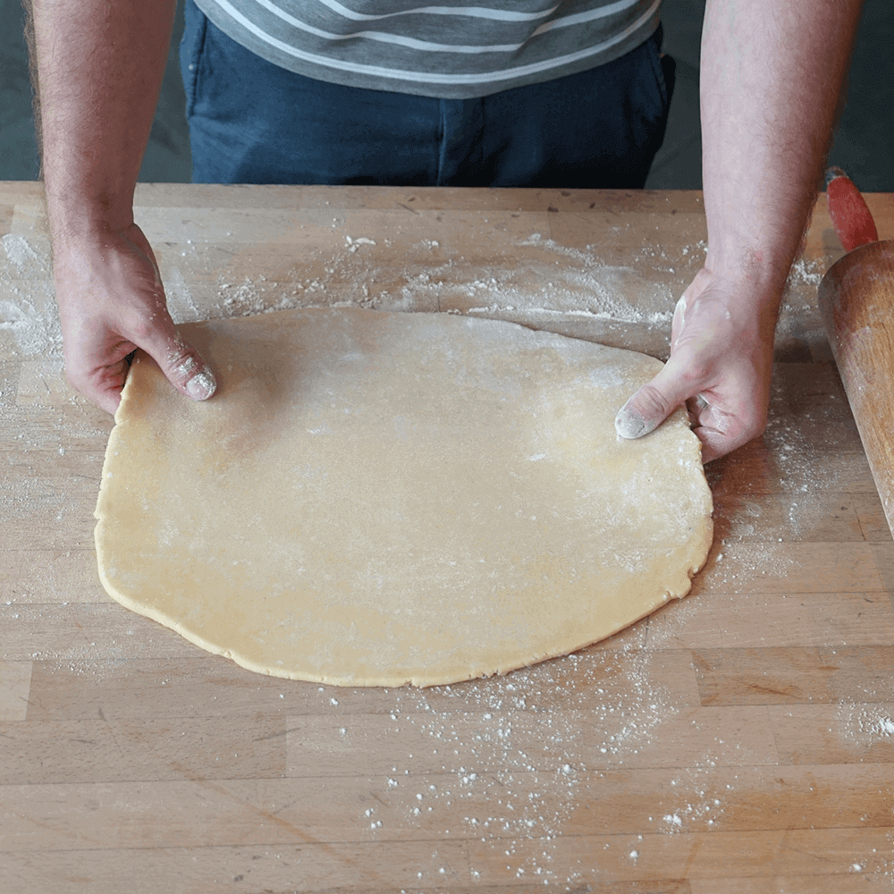 Ausstechmatten für die Plätzchenproduktion Zwei Hände bereiten einen Plätzchenteig auf einer Holzarbeitsplatte vor.