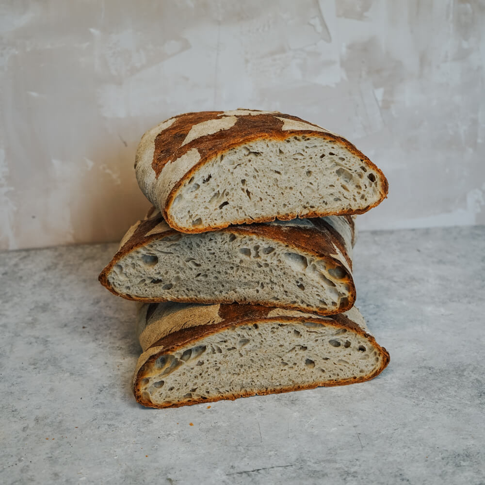 Rezept für XXL-Brot XXL-Brot in 3 Teile geschnitten, aufeinander gestapelt und vor einem hellgrauen Hintergrund