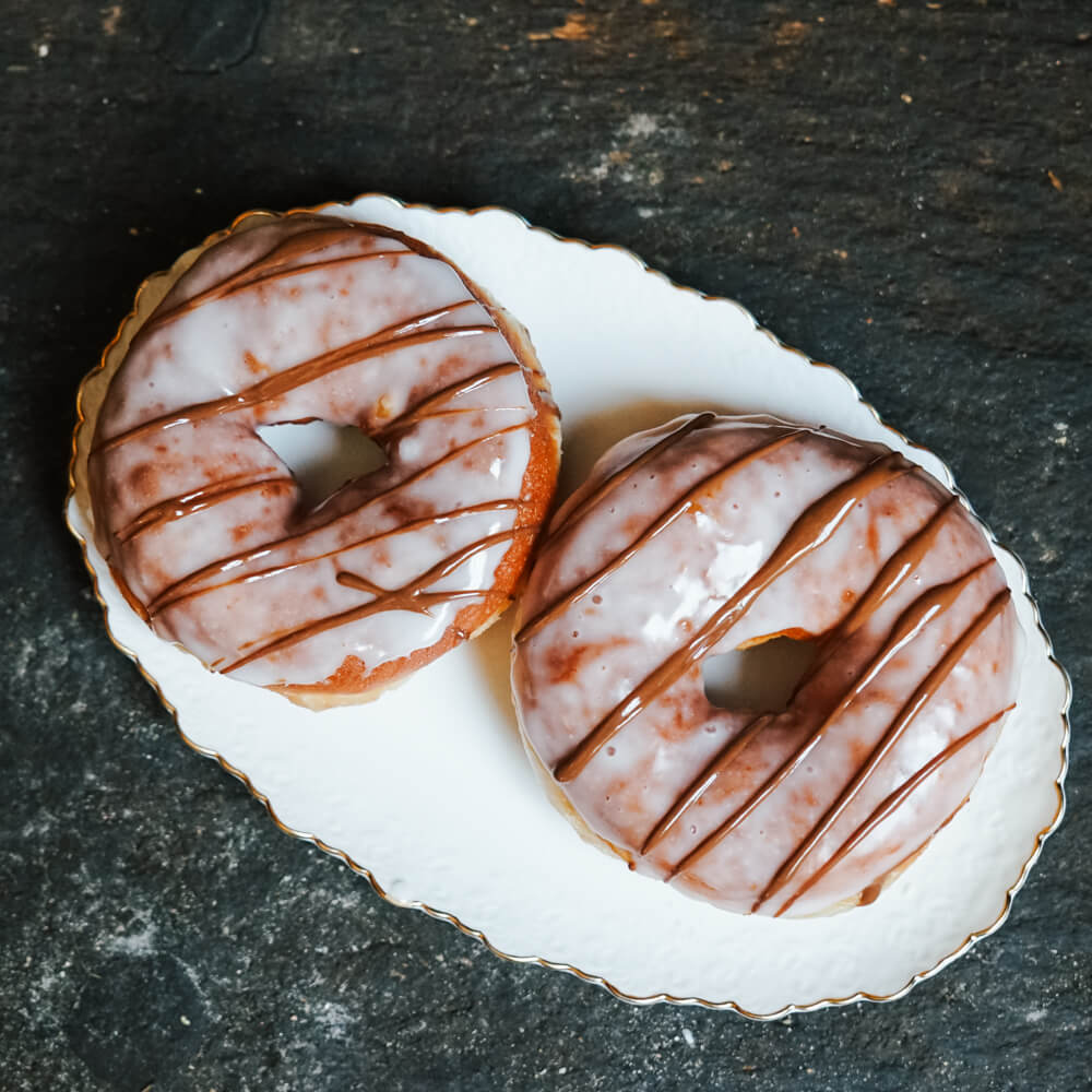 Rezept für Donuts Zwei Donuts mit Zuckerguss und Schokolade auf einem weißen Teller serviert