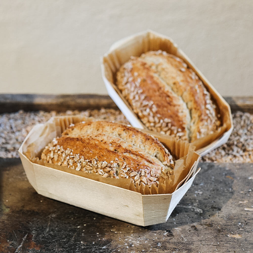 Rezept für Adelindes Rustikales Dinkelbrot mit Saaten selbstgemachtes Dinkelbrot mit Saaten in einer Holzbackform gebacken und serviert mit Körnern im Hintergrund