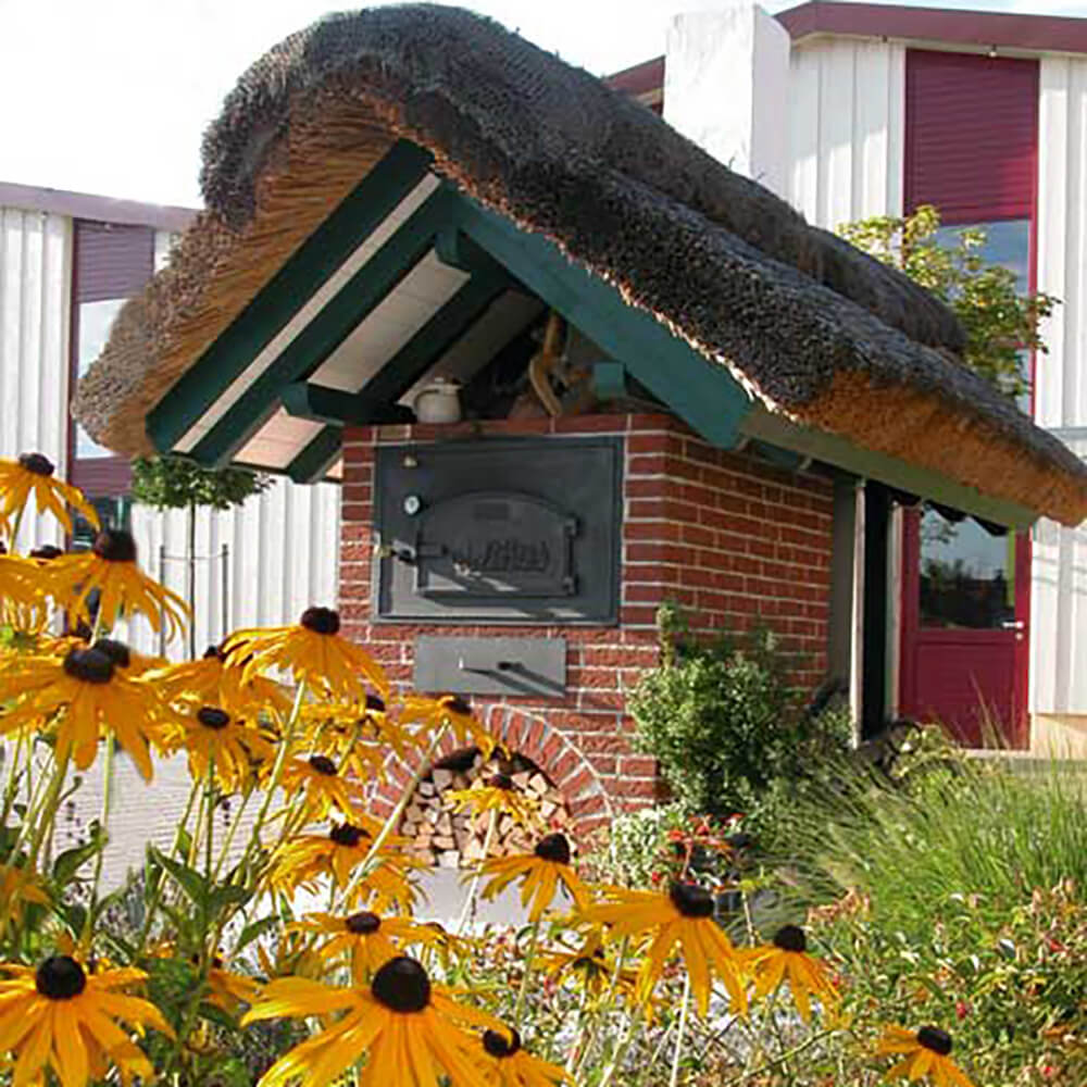 Bausatz HABO - Türmodell C Aufgebauter HABO Bausatz zu einem schönen Backhäuschen mit einem Strohdach vor einigen Blumen.