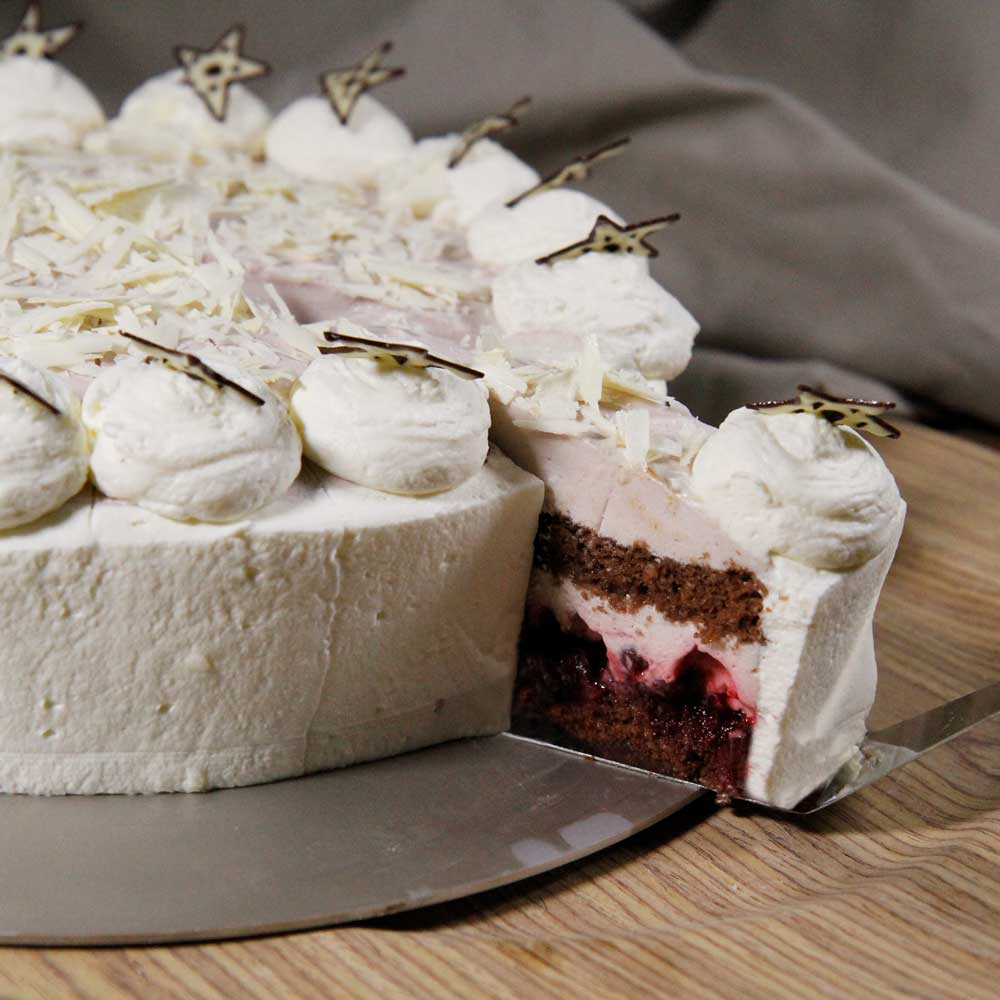 Eine mit Sahnehäufchen dekorierte Glühweintorte. Sie wurde angeschnitten und ein Stück wird gerade mit einer Tortenschaufel angehoben.