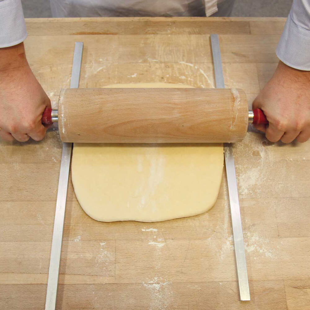 Ausrollhilfen mit Wellholz und Teig der ausgerollt wird auf einer hölzernen Arbeitsfläche