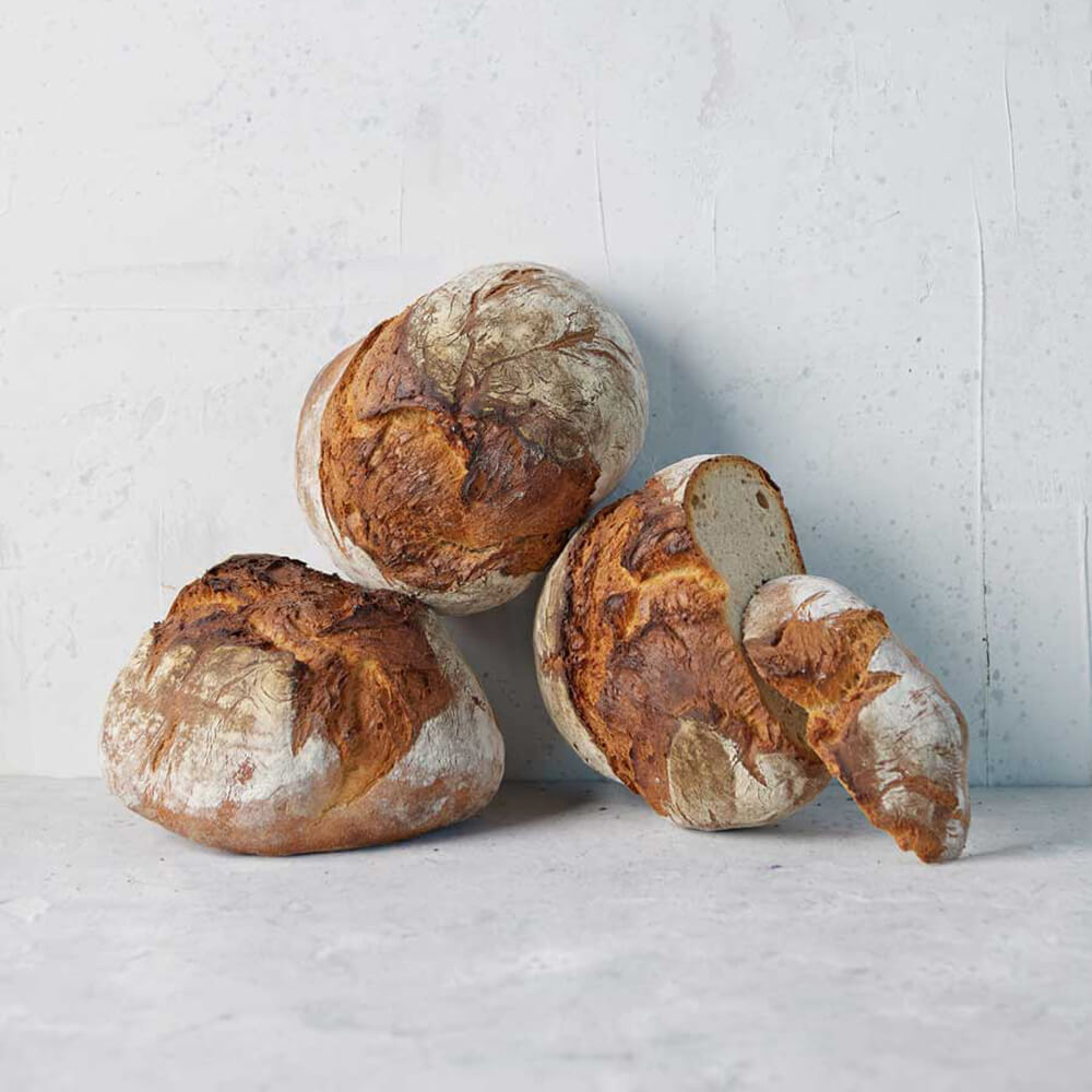 Bauernbrot-Backmischung mit Gärkorb - Set Drei Bauernbrotlaibe. Ein Laib ist aufgeschnitten.