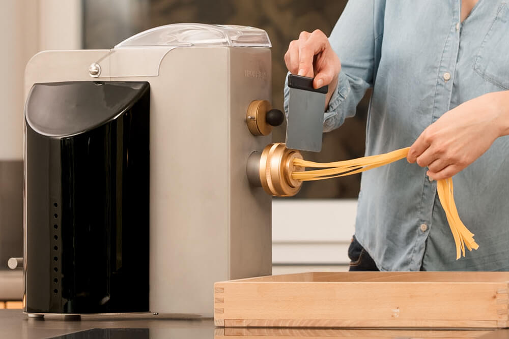 Nudelmaschine EMMA in Betrieb - frischer Nudelteig wird durch Walzen gedrückt, traditionelle Pasta-Herstellung.
