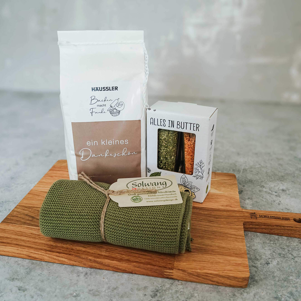 Geschenk-Set mit mehlmischung, Buttergewürz, Geshcirrtuch und Holzbrett vor einem Steinhintergrund 