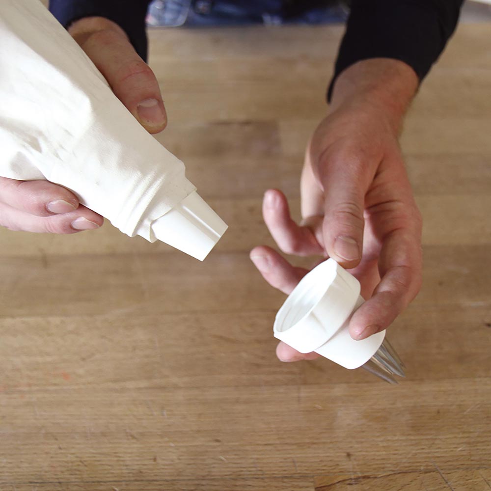 Spritzbeutel-Adapter Spritzbeutel-Adapter wird von zwei Händen über einer hölzernen Arbeitsplatte gehalten