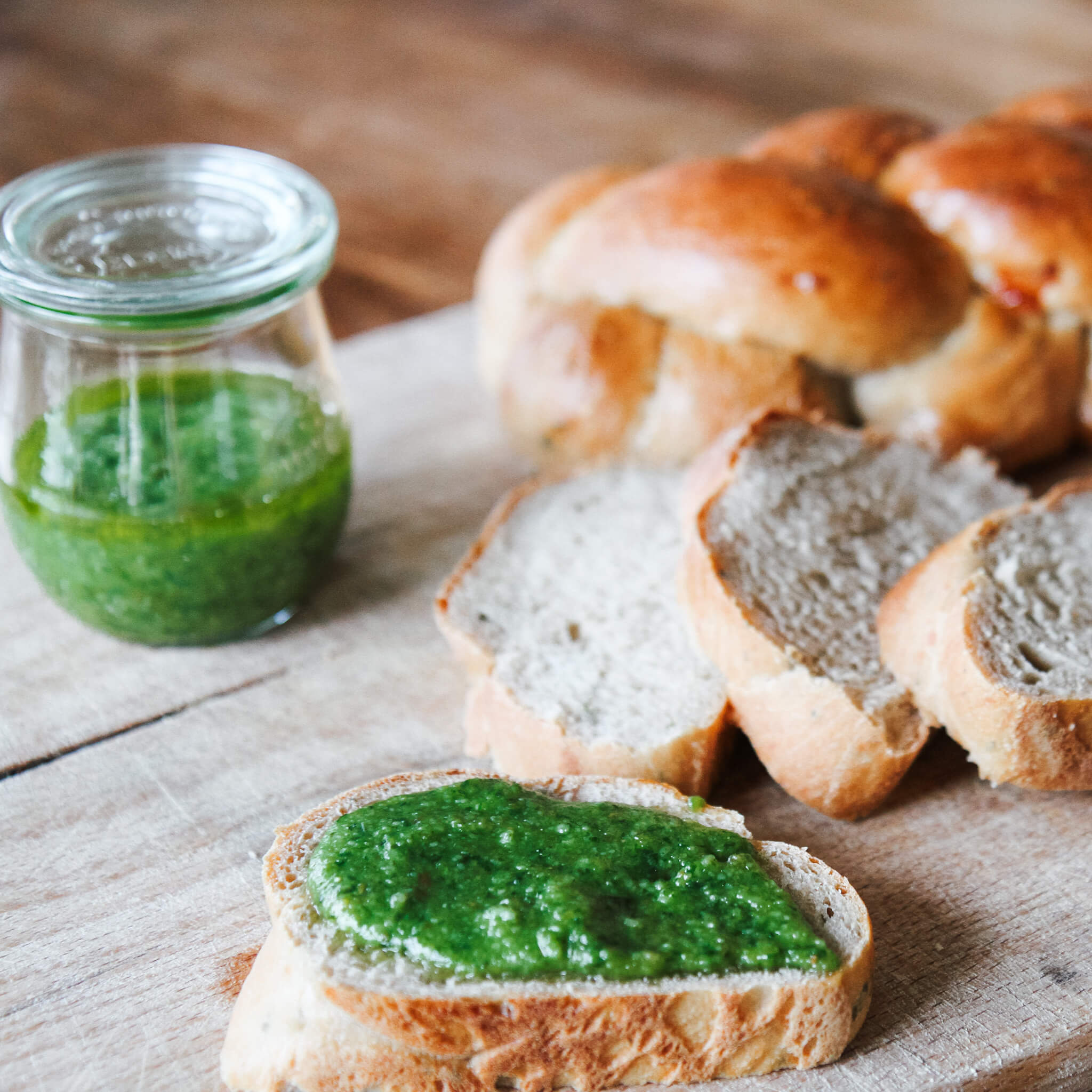 Rezept für Kräuterzopf Kräuterzopf mit frischen Kräutern und Käsewürfeln drin und passen dazu grünes Basilikumpesto in einem Weckglas auf einem Holzbrett serviert