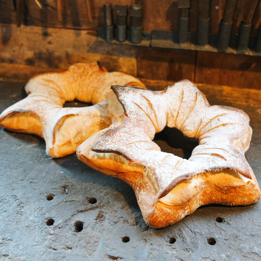 Rezept für Sternbrot mit Dinkelmehl 2 Brote in SSternform mit Mehl bestreut auf einer dunklen Platte