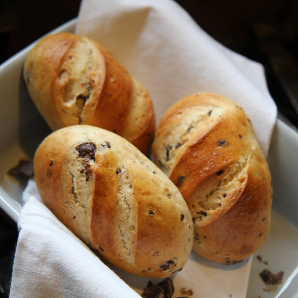 Rezept für Schokobrötchen 3 selbstgemachte Schokobrötchen in einer weißen Schale mit einem Weißen Tuch serviert und mit Schokostreuseln dekoriert