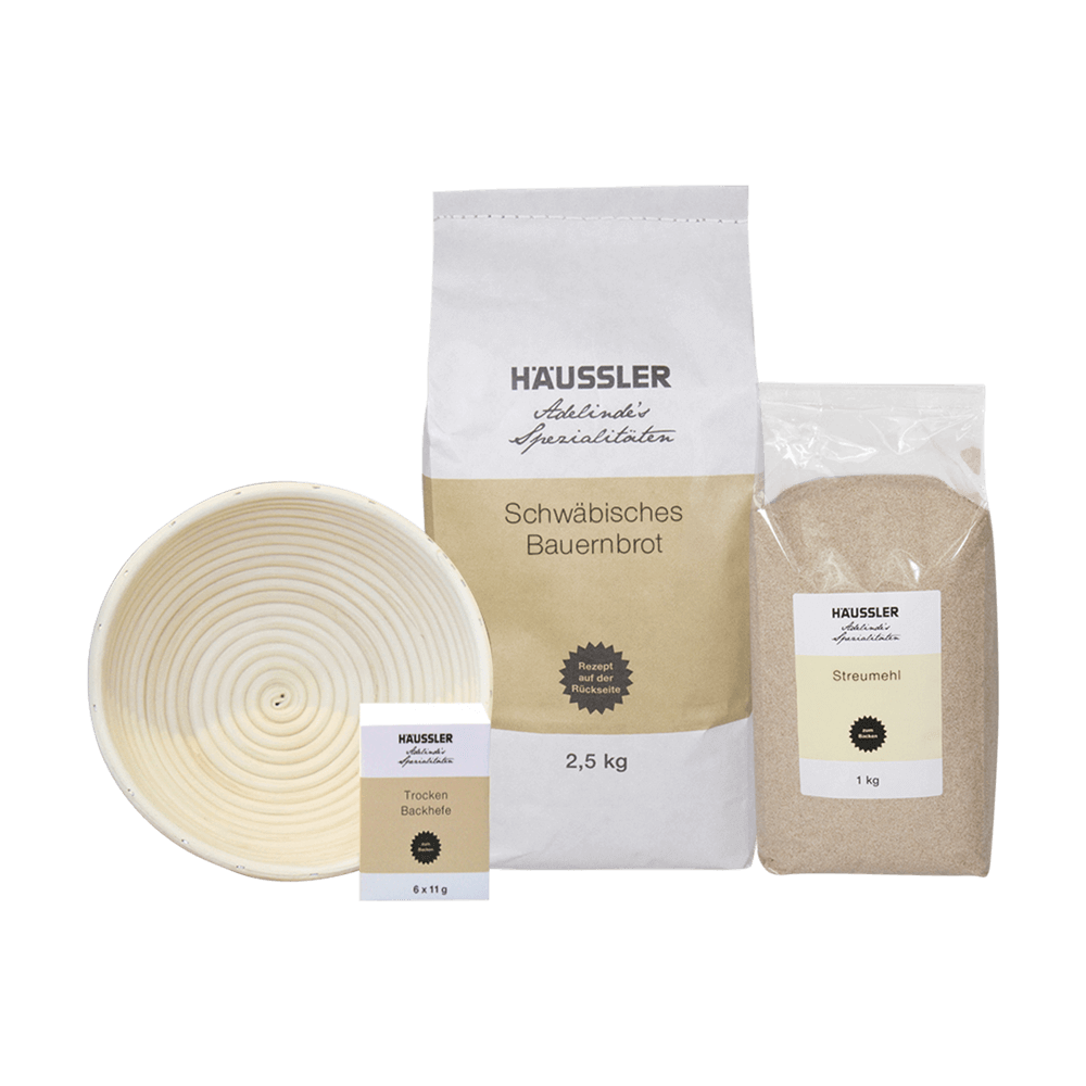Schwäbisches Bauernbrot mit Gärkorb Weiße Verpackung mit beigem Aufkleber und der Aufschrift Schwäbisches Bauernbrot 2,5 Kilogramm. Zudem befindet sich auf dem Bild ein Peddigrohrkorb, Trockenbackhefe 6 x 11 Gramm und Streumehl 1 Kilogramm.