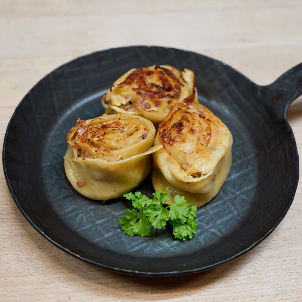 Rezept für Krautkrapfen 3 Krautkrapfen aus Nudelteig und einer Füllung mit Sauerkraut und Kassler in einer Gusseisernen Bratpfanne serviert mit Petersilie