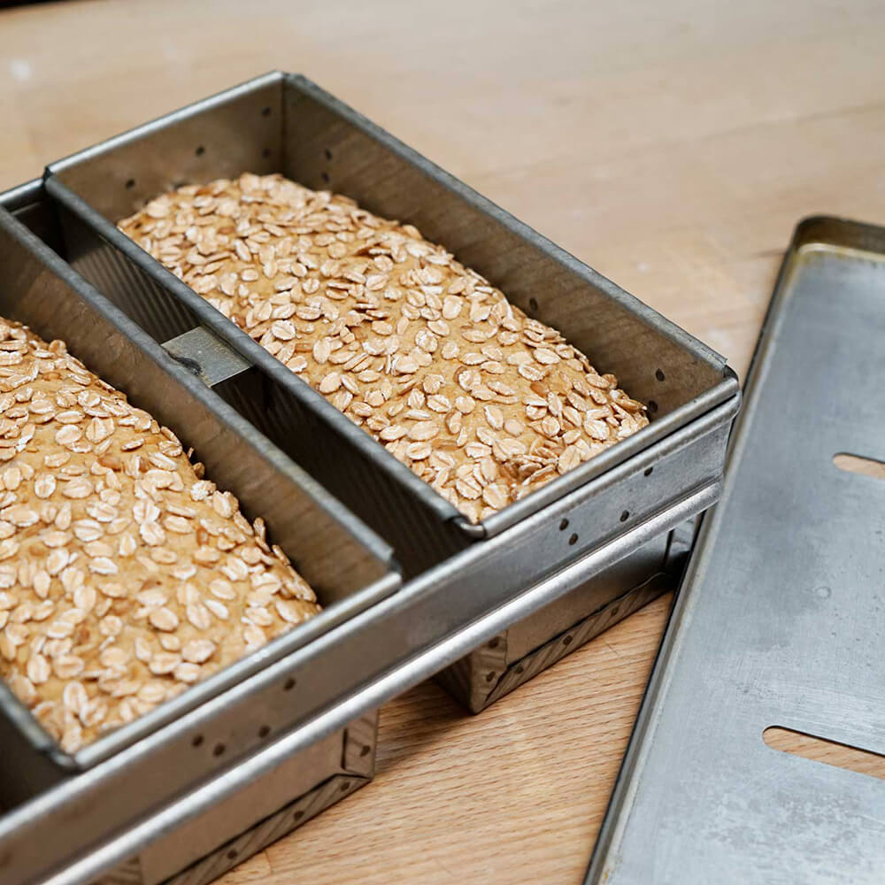 Ausschnitt der 4-teiligen Toastbrotform. 2 Einzelformen sind mit einem Vollkornbrot gefüllt. Die Form steht auf einer Arbeitsfläche