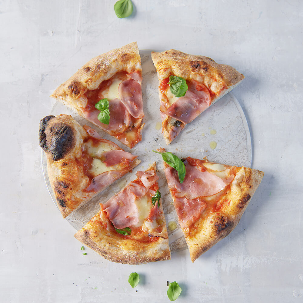 Rezept für Adelindes Pizza frische gebackene Pizza, belegt mit passierten Tomaten, Schinken, Käse und frischem Basilikum in 5 Stücke geschnitten