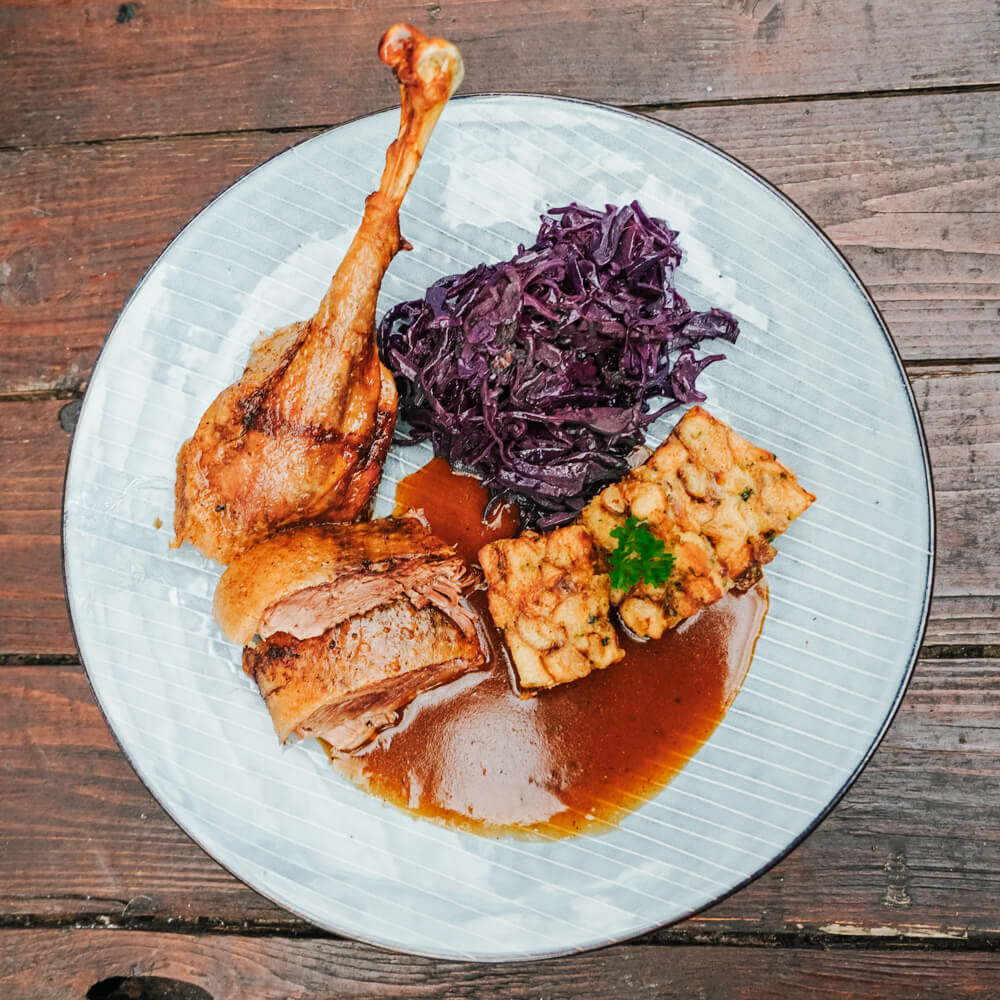 Rezept für Weihnachtsgans Weihnachtsgans mit Blaukraut und Brezelknödel auf einem hellblauen Teller angerichtet mit einer Soße