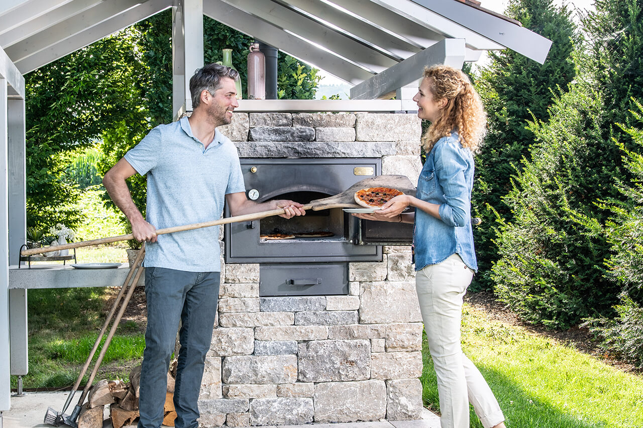 Paar backt Pizza an einem Backhäuschen