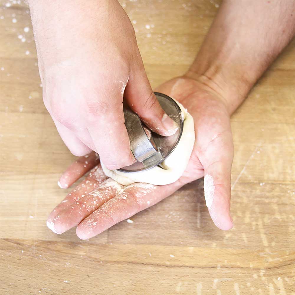 Brötchendrücker Zu sehen sind zwei Hände die den Brötchendrücker abwenden. In der einen Hand liegt der Brötchenteig und die andere Hand drückt den Brötchendrücker in den Teig.