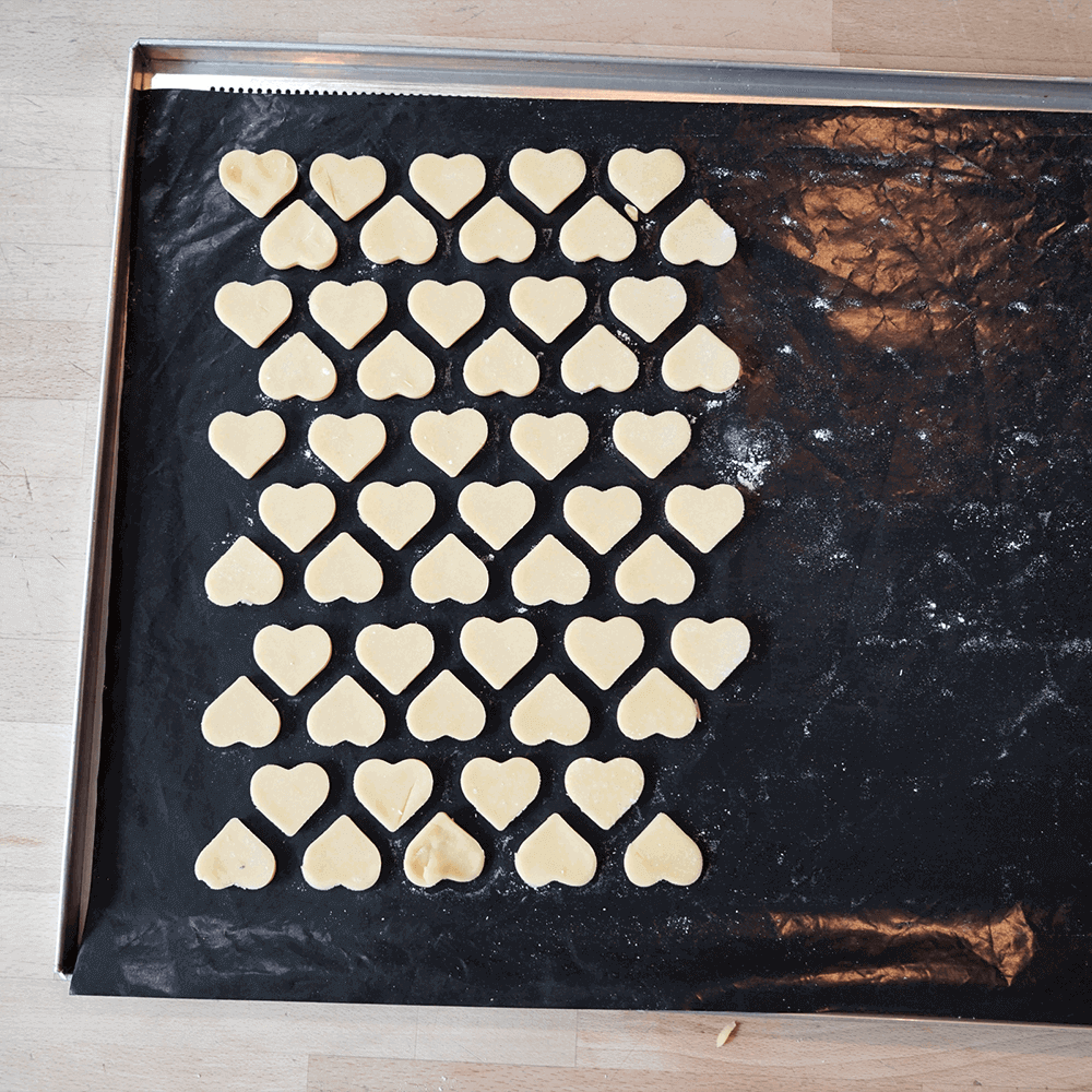 Ausstechmatten für die Plätzchenproduktion EIn Backblech mit schwarzer Dauerbackfolie. Darauf liegen ausgestochene Herzen aus Plätzchenteig