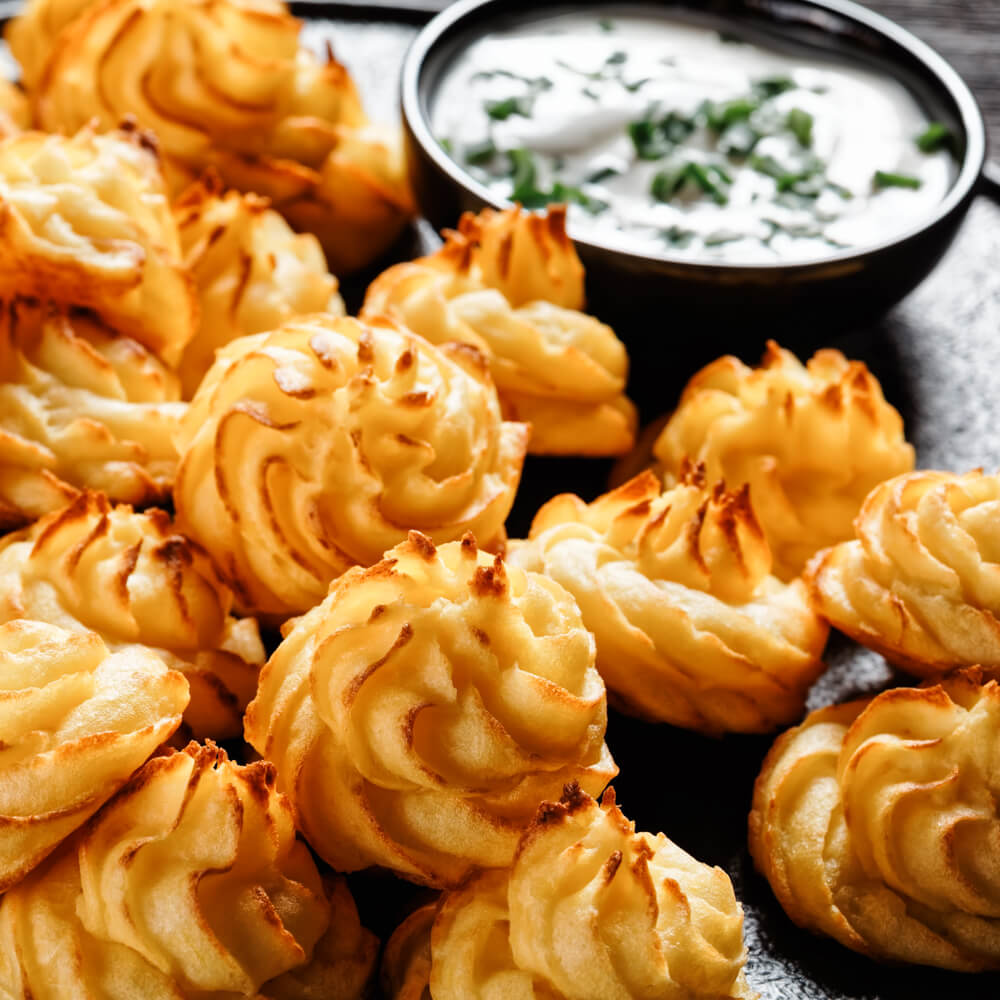 Rezept für Herzogin Kartoffeln goldbraun gebackene Herzogin Kartoffeln auf einem schwarzen Teller mit Kräuterdip