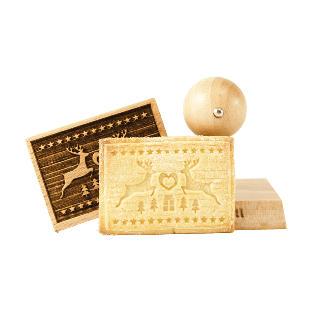 Keksstempel Keks mit zwei aufeinander zuspringenden Rentieren. In der Mitte ist ein Herz und darunter zwei Tannenbäume, ein Geschenk und nochmal zwei Tannenbäume. Eingerahmt ist das Motiv mit einer Sternenleiste. Im Hintergrund steht ein Stempel und der Stempelkopf