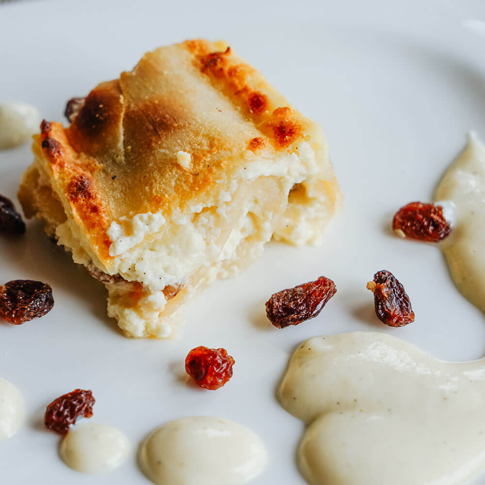 Rezept für Apfel- und Topfenstrudel ein Stück Topfenstrudel mit Rosinen und ein wenig Vanillesoße auf einem weißen Teller serviert
