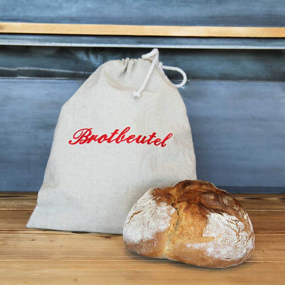 Brotbeutel mit Kordel und rotem Schriftzug "Brotbeutel" mit einem frisch gebackenen Brot im Vordergrund