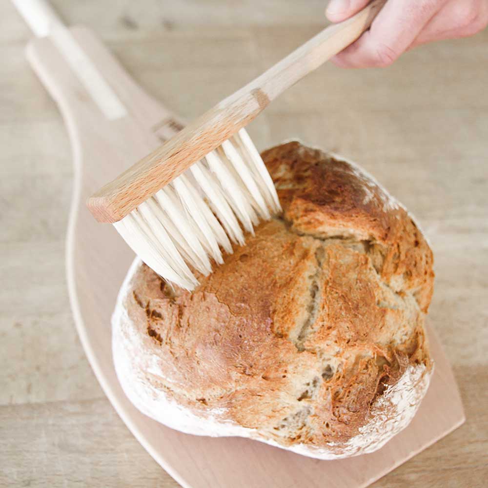 Brotpinsel zum Einstreichen der Brote mit Wasser Ein ausgebackenes Brot auf einem Backschieber welches mit dem Brotpinsel angefeuchtet wird