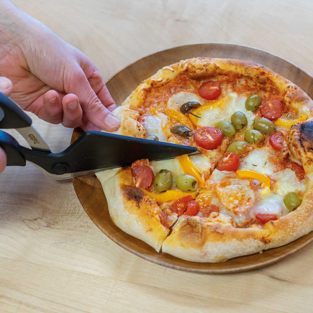 Pizzaschere Eine Person schneidet eine frisch gebackene Pizza mit der Pizzaschere in einzelne Stücke, auf einer Küchenarbeitsplatte.