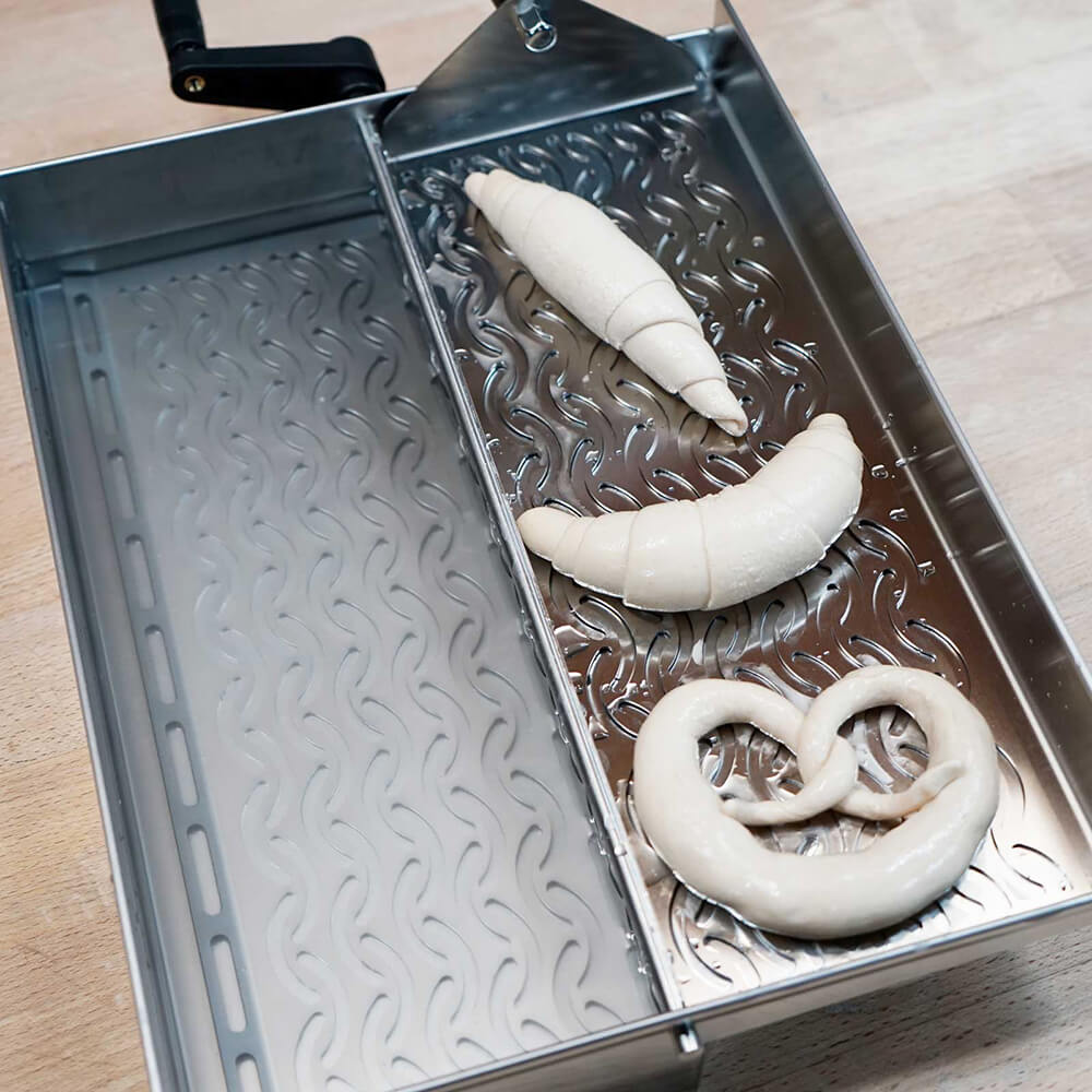 Belaugungsgerät Das Belaugungsgerät in der Anwendung, die belaugten Teiglinge liegen auf der Abtropfläche. Das Gerät steht auf einer Arbeitsplatte.