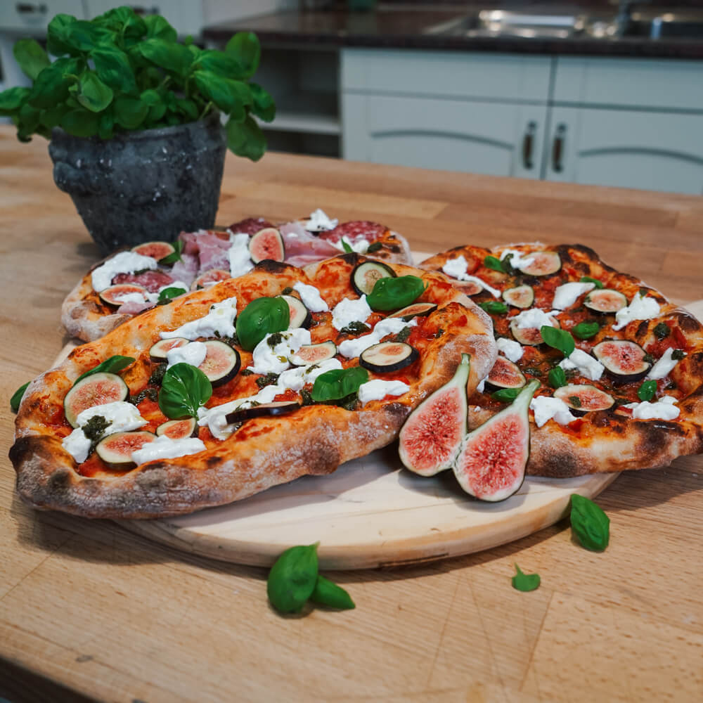 fluffige Pinsa mit Tomatensoße, Burrata, frischen Feigen und Basilikum auf einem Holzbrett serviert