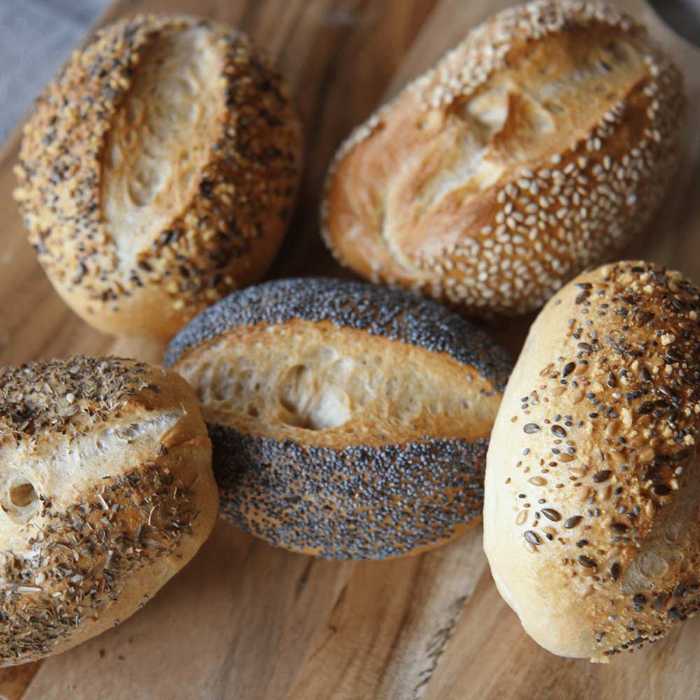 5 Wecken mit Mohn, auf einem Holzbrett liegend, abgebildet