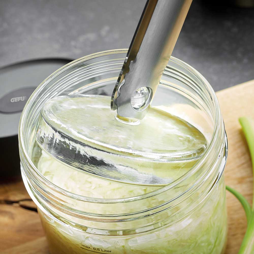 Fermentierglas, bei welchem mit der Zange der Glasdeckel angeboben wird auf in einer Küche.