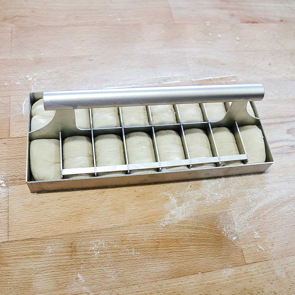 Teigteiler eckig Abstechwerkzeug befindet sich in dem Teig, sodass die einzelnen Teiglinge ersichtlich werden, auf einer Küchenarbeitsplatte.