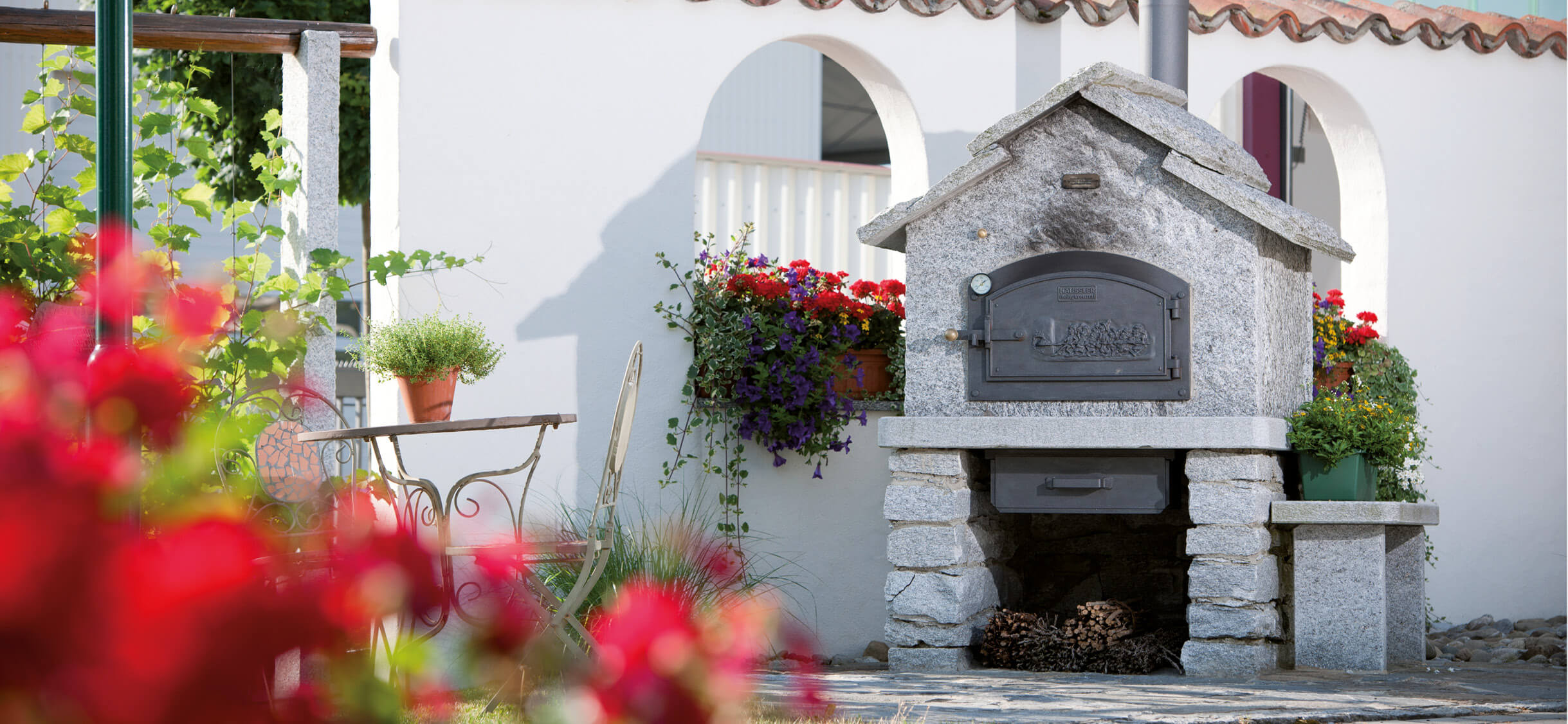 Weisses_Backhäuschen Weißes Backhäuschen im idyllischen Innehof des Backdorfs, umgeben von rustikalen Mauern und blühenden Pflanzen