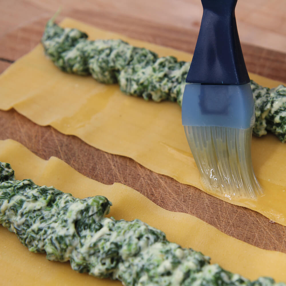 Rezept für Cannelloni mit Spinat-Ricottafüllung Teigplatten mit einer Spinat-Ricottamasse die mit einem Pinsel mit Ei eingestriechen werden um diese zusammen zu rollen