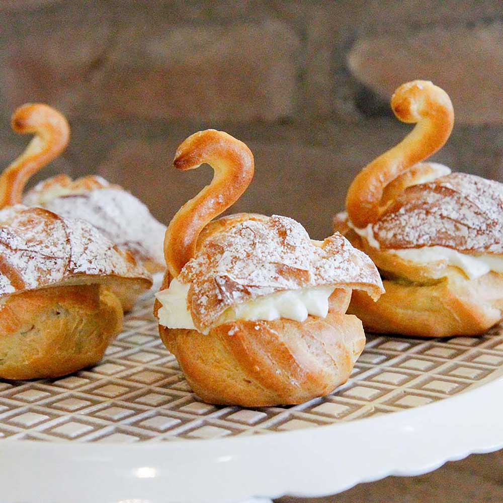 5-teiliges Lochtüllenset Windbeutel in Form von einem Schwan. Sie sind mit Sahne gefüllt und mit Puderzucker bestreut.