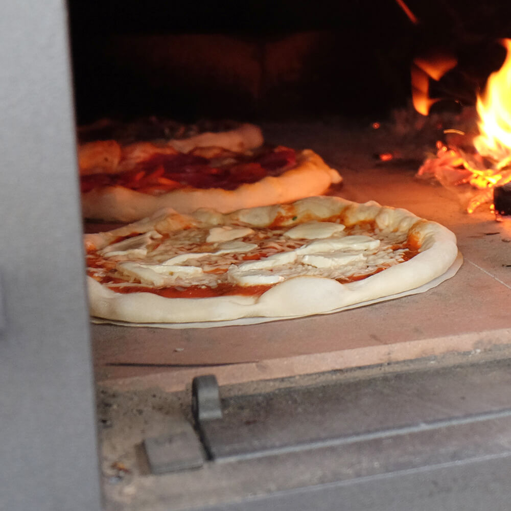 Backpapier rund zum Backen auf Schamottestein Belegte, runde Pizza auf rundem Backpapier auf einem Schamottestein in einem Ofen, der mit Holz befeuert wurde.