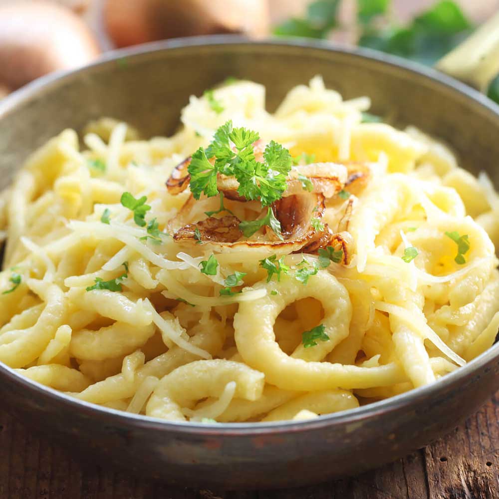 Frische Käsespätzle in einer Schale mit Röstzwiebeln und Petersilie.