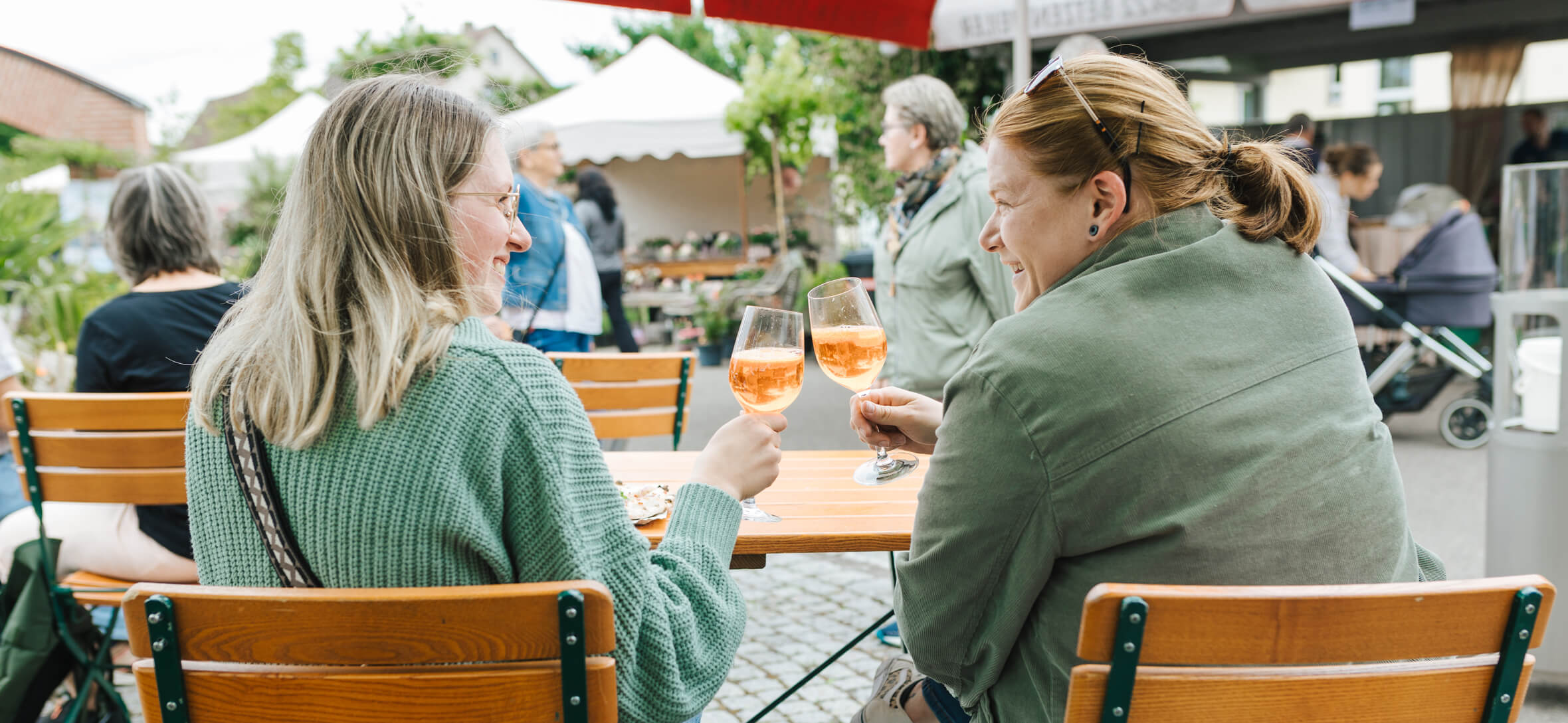 Sommerliche Stimmung beim Brotfest. Zwei junge Frauen stoßen mit Getränken im Innenhof des Backdorfs miteinander an - sommerliche Stimmung beim Brotfest.