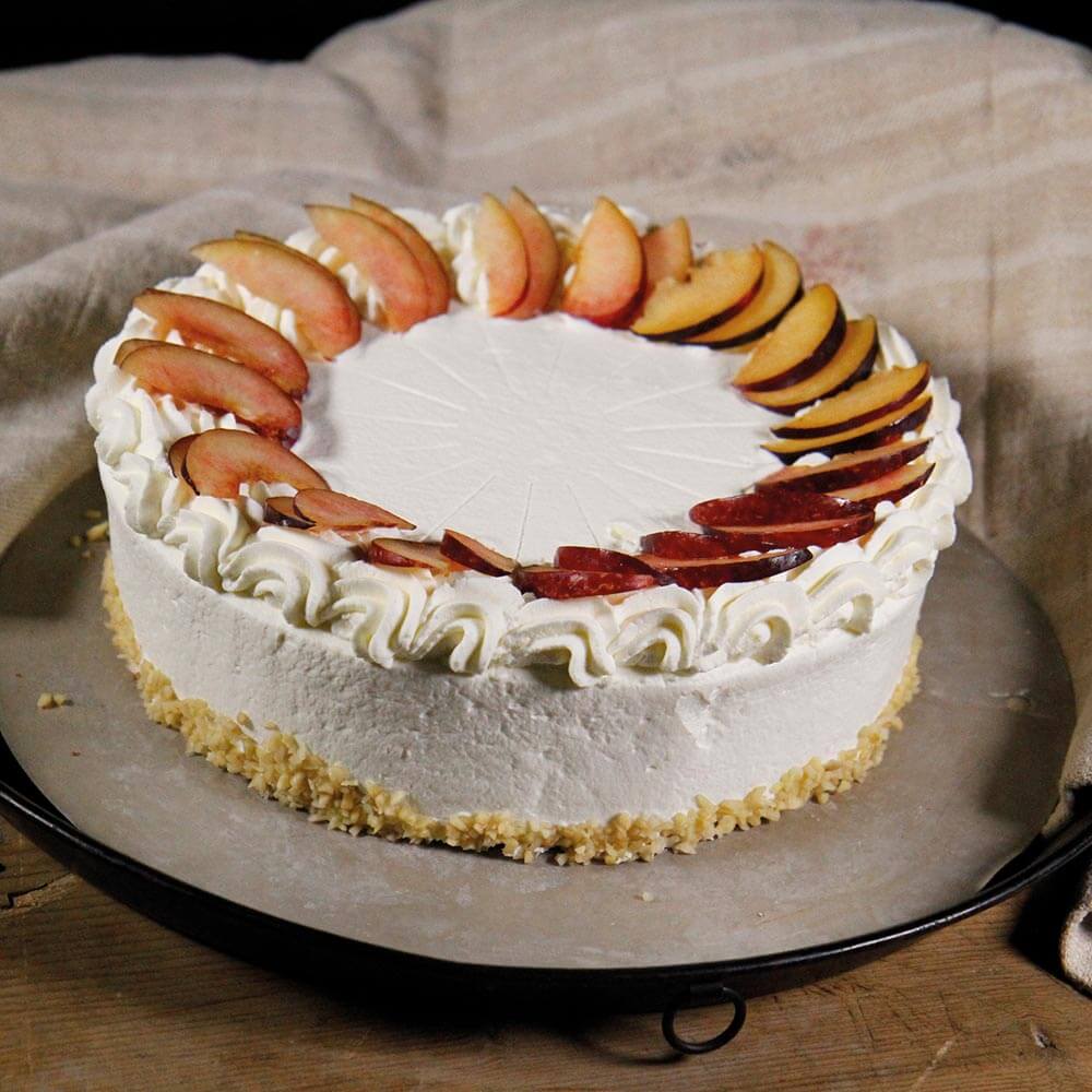 Ein Kuchen mit Früchten steht auf einer Edelstahltortenplatte auf einem braunen Tisch