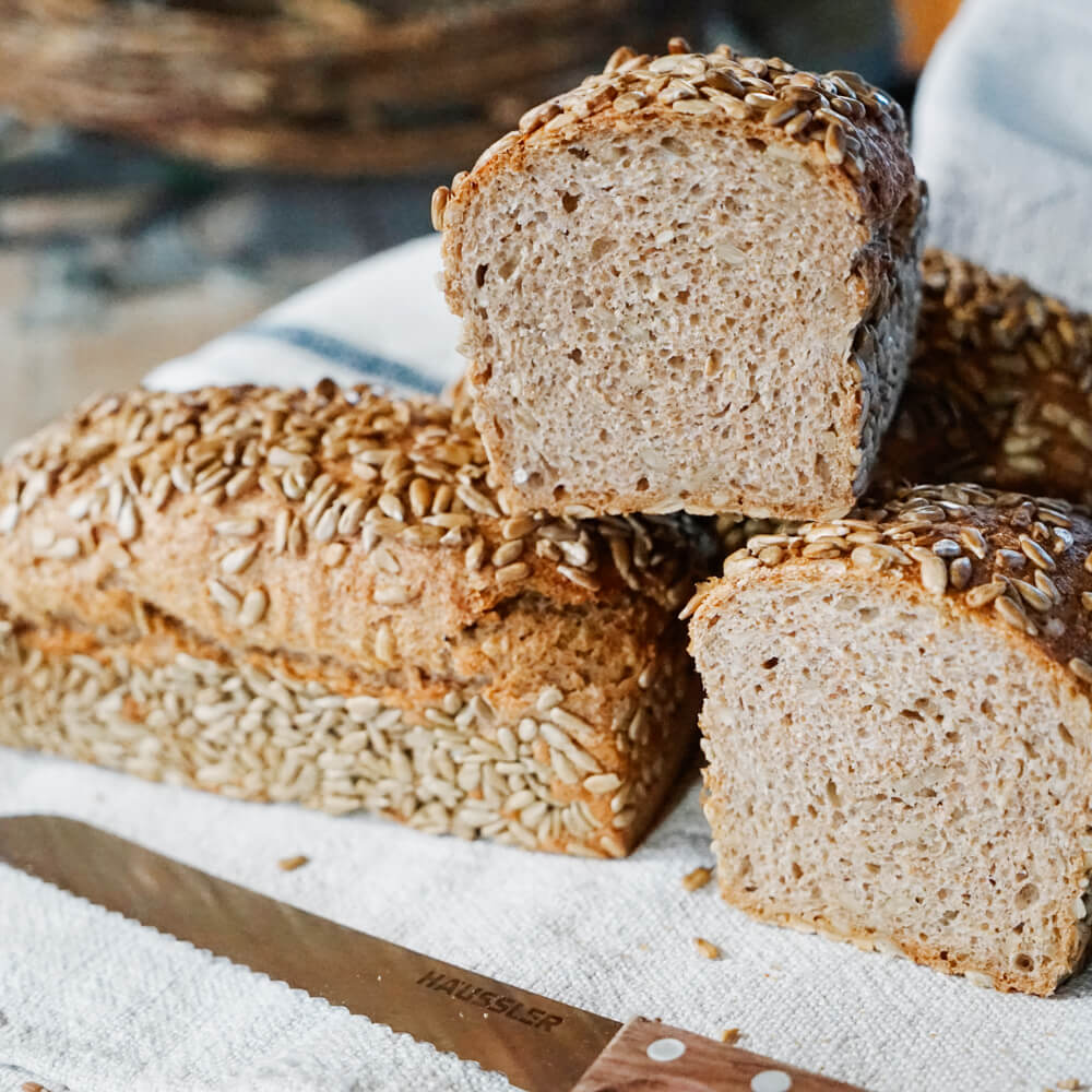 3 Dinkelvollkronbrote aufeinander gestapelt mit einem Brotmesser im Vordergrund