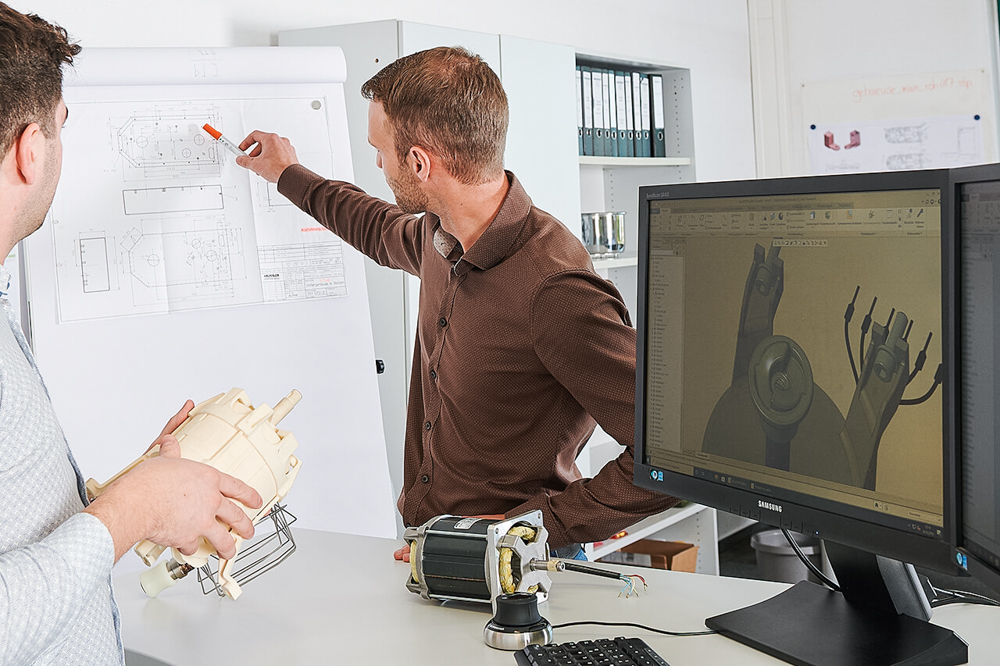 Häussler_Produktentwicklung Mitarbeiter arbeiten konzentriert an einem Konstruktionsbrett, mit technischen Zeichnungen und Planungsunterlagen vor sich.