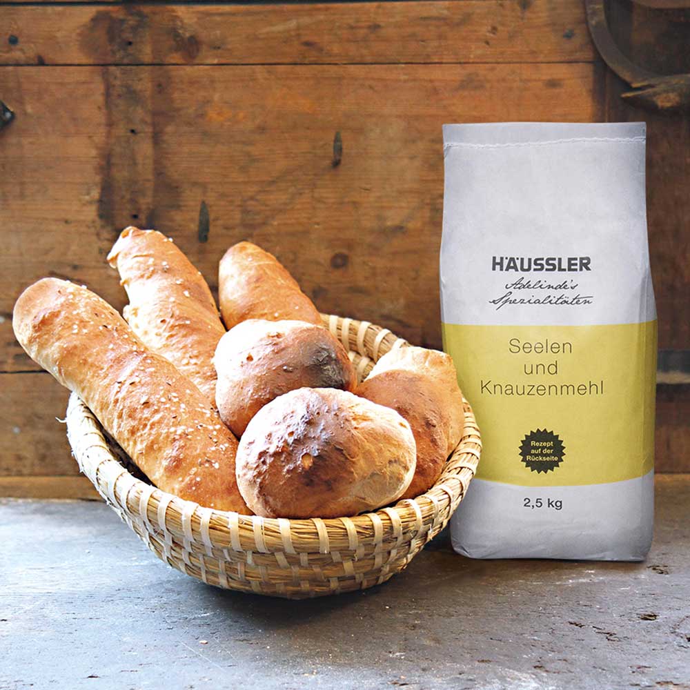 Seelen- und Knauzenmehl Seelen- und Knauzenmehl in einer 2,5 kg Packung neben einem Korb, der mit frisch gebackenen Seelen und Knauzen gefüllt in einer Küche.