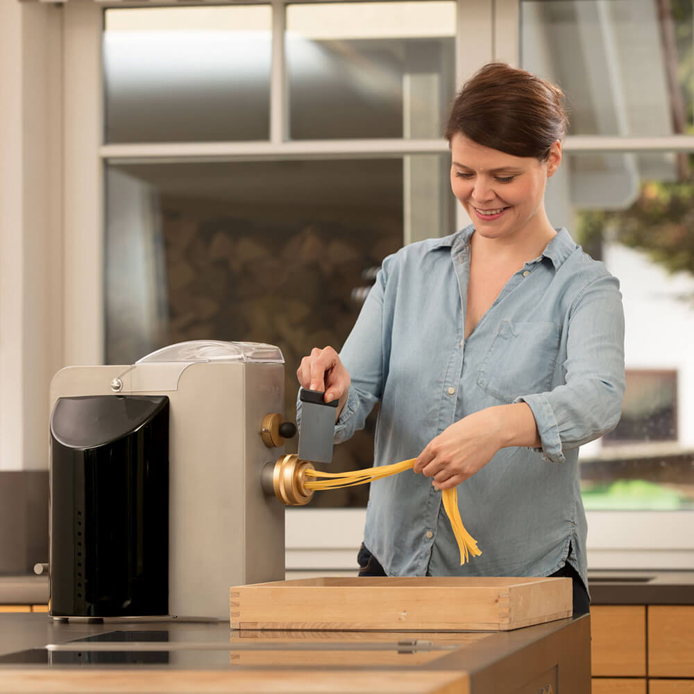 Nudelmaschine Emma Nudelmaschine mit der gerade Nudeln gemacht werden. vor der Nudelmaschine befindet sich eine Nudelhorde.