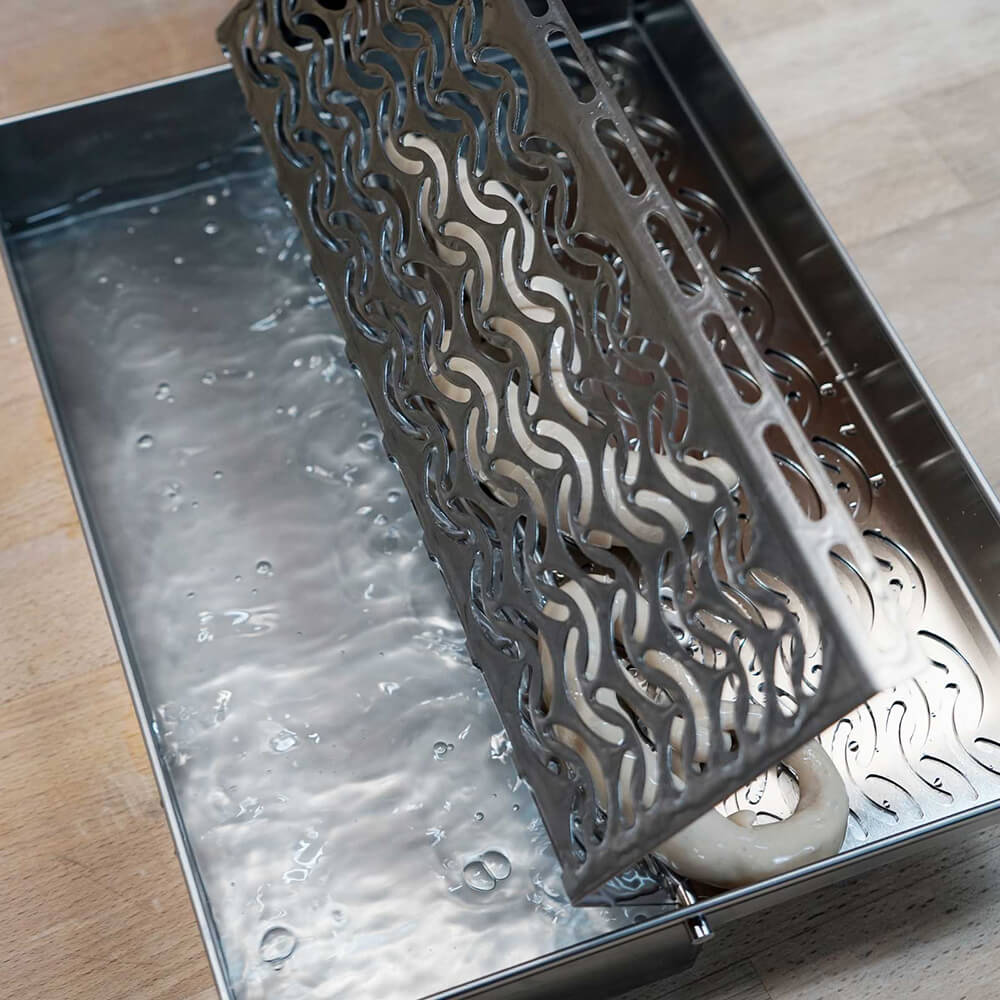 Belaugungsgerät in der Anwendung, die belaugten Teiglinge werden gerade auf die Abtropffläche gekippt. Das Gerät steht auf einer Arbeitsplatte.