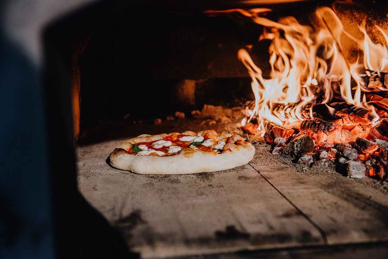 Pizza liegt vor dem Feuer in einem Holzbackofen